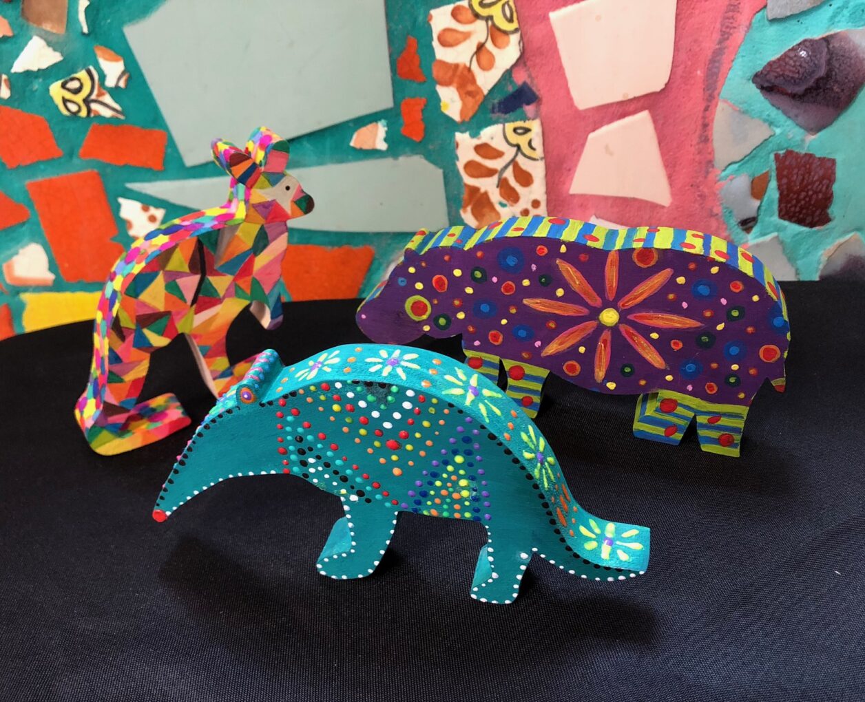 Three small wooden animals - a kangaroo, an aardvark, and a hippo - are adorned with bright colors and patterns