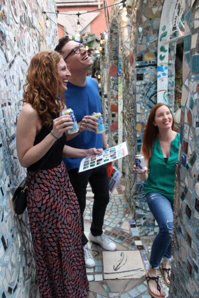 A group of three adults smile as they challenge themselves with a tile scavenger hunt at Philadelphia's Magic Gardens