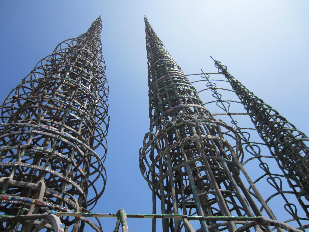 Three tall spires made from rebar, cement, and decorated with tile. The spires reach up towards a blue sky.
