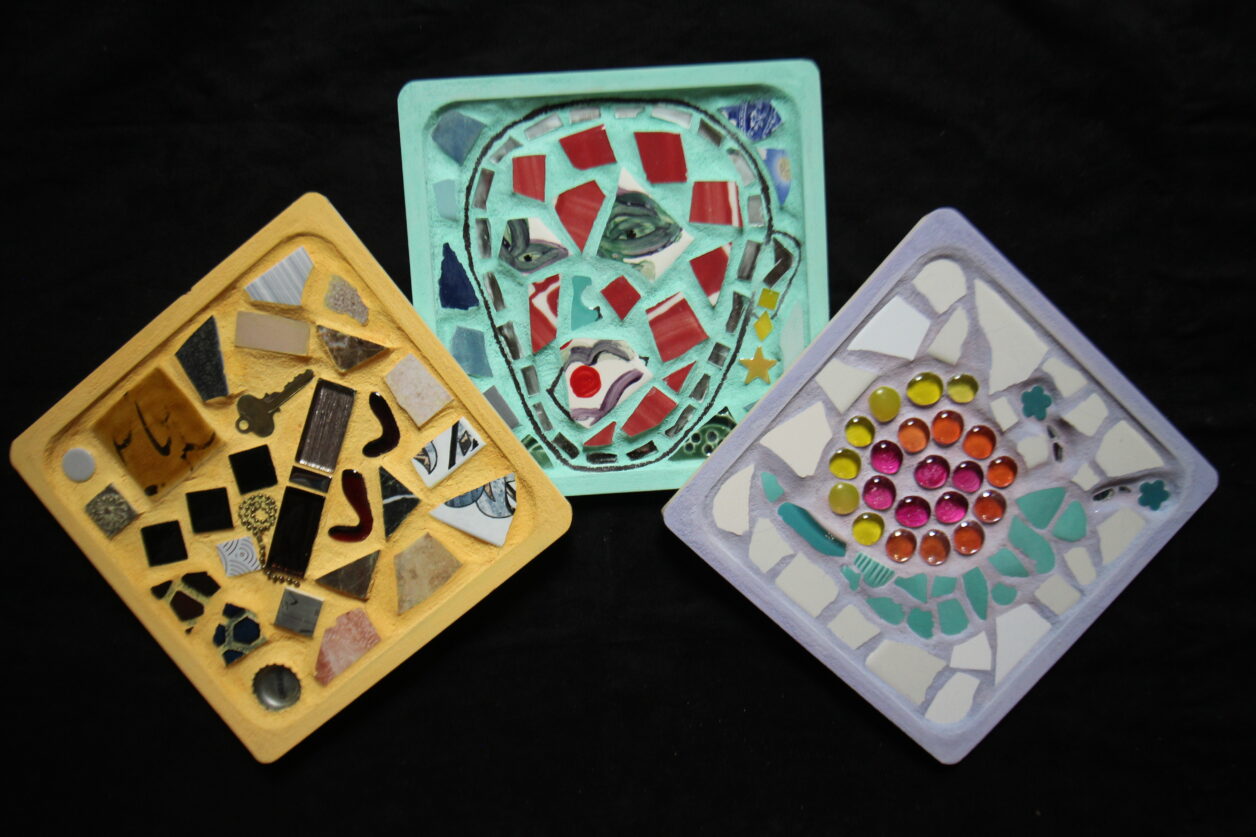 Three small, square mosaics made out of colorful tiles and glass.