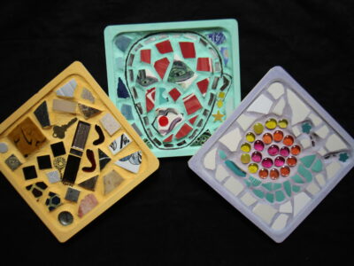 Three small, square mosaics made out of colorful tiles and glass.