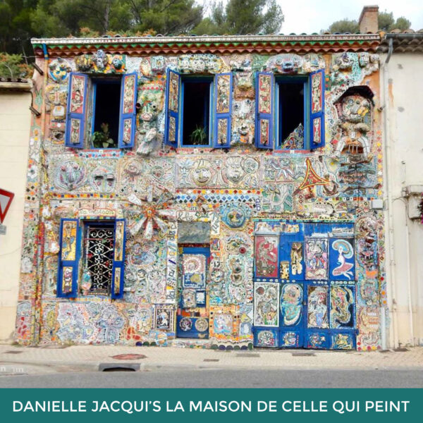 Danielle Jacqui’s La Maison de Celle Qui Pein. The front façade of a building is covered in mosaicked tiles and the shutters are painted in a variety of colors.