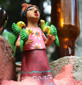 Mexican folk art at Philadelphia's Magic Gardens. A small ceramic woman wearing a pink dress has colorful parrots on her arms.