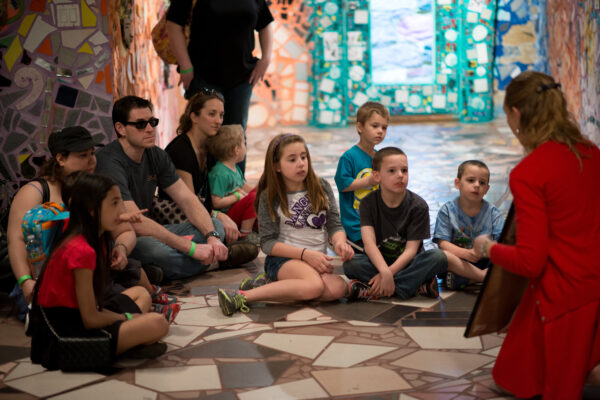 Children and adults sit around a tour guide in Philadelphia's Magic Gardens' mosaicked basement.
