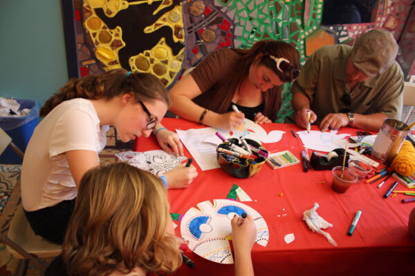 A group of children and adults sit around a craft table coloring in a gallery at Philadelphia's Magic Gardens.