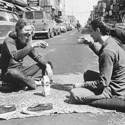 A black and white photo of Isaiah Zagar and a friend picnicking in the middle of South Street in 1968.