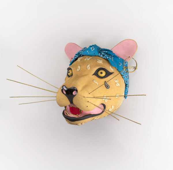 A ceramic jaguar head wearing a turquoise bandana, with gold whiskers, gold earrings, and gold teeth.