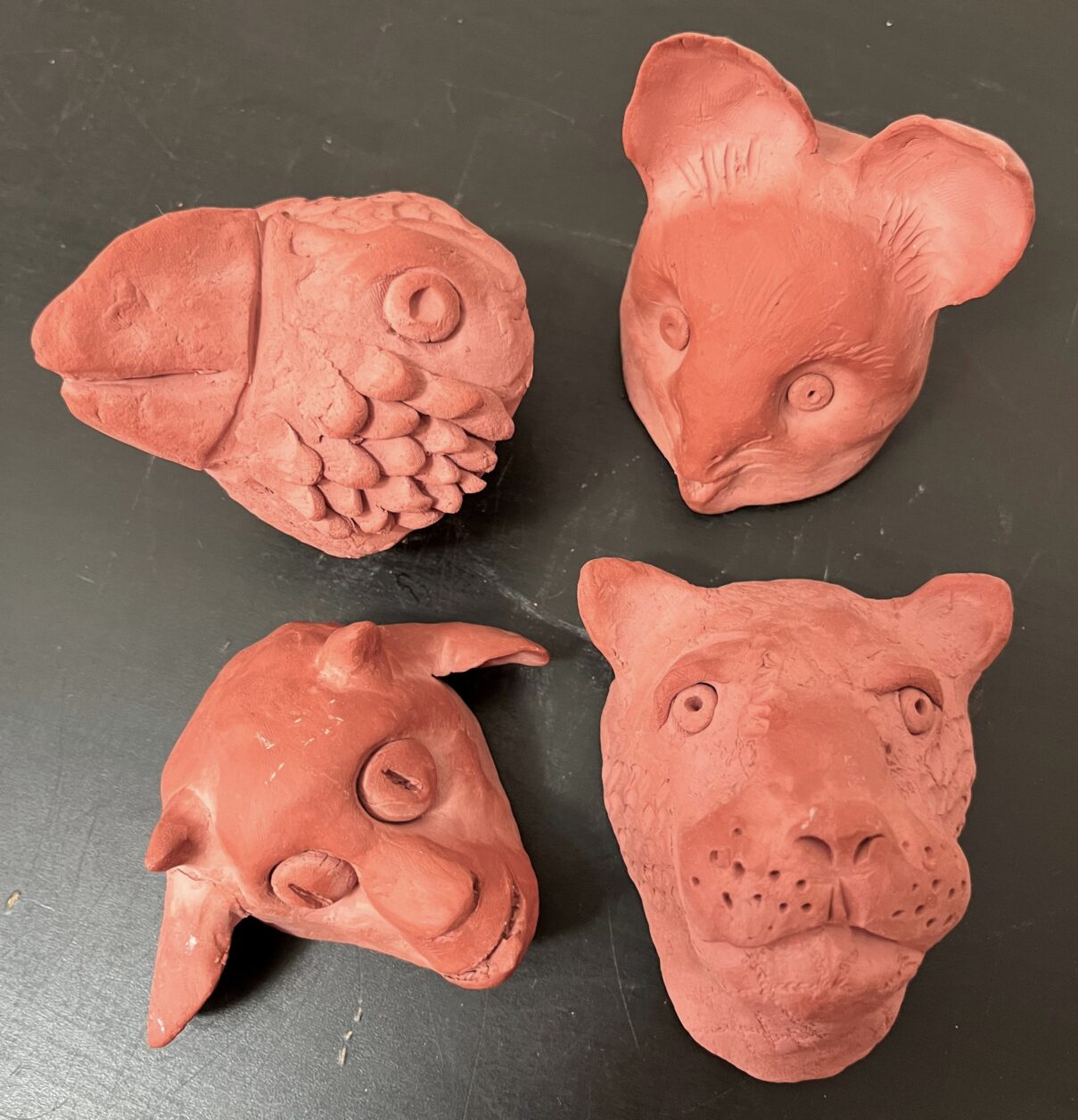 Four unpainted, sculpted clay animal heads - a bird, mouse, goat, and jaguar.