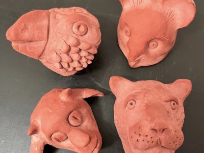 Four unpainted, sculpted clay animal heads - a bird, mouse, goat, and jaguar.