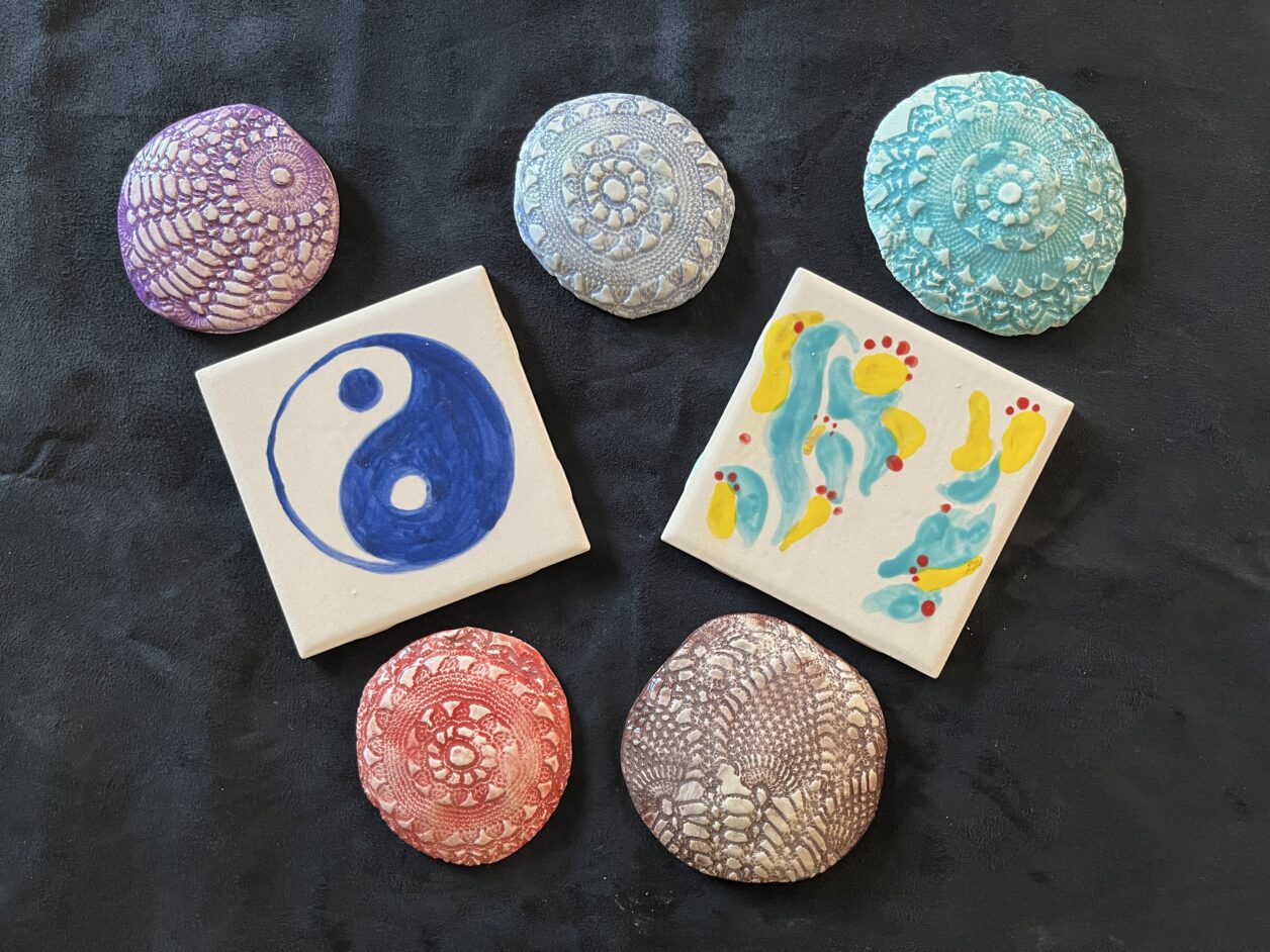 Five round "doily" tiles in various colors and two square tiles with various painted designs on them.