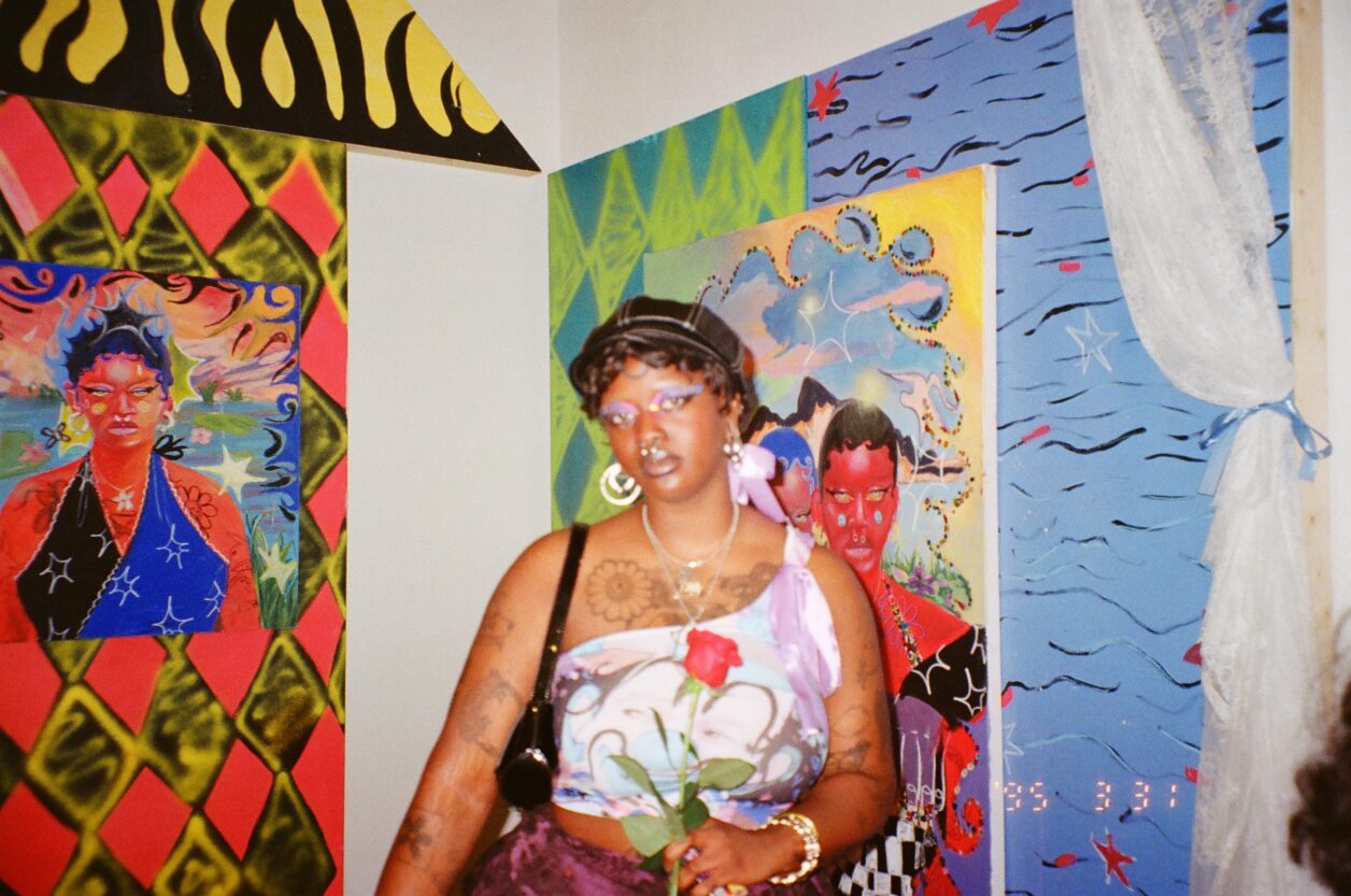 Photograph of Zeinab Diomande, a young Black woman, in front of two of her paintings