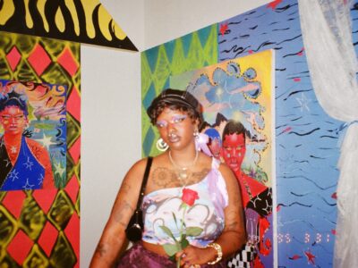 Photograph of Zeinab Diomande, a young Black woman, in front of two of her paintings