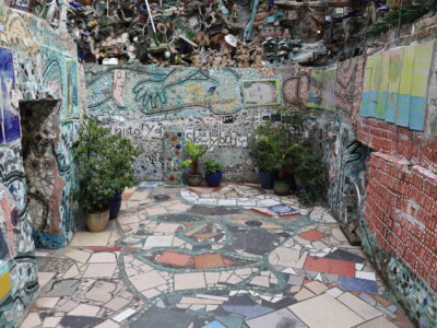 A view of a walled-in mosaicked portion of Philadelphia's Magic Gardens. Potted plants are placed in the corners.