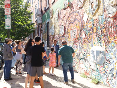A tour guide speaks to a group about a mosaicked mural on a street near Philadelphia's Magic Gardens.