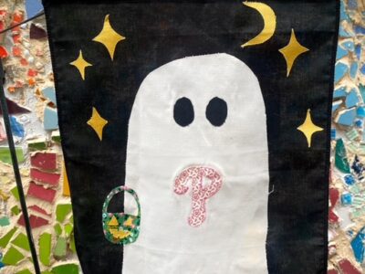 A black flag with a white ghost on it. The ghost has the Phillies symbol on its chest and gold stars around its head.