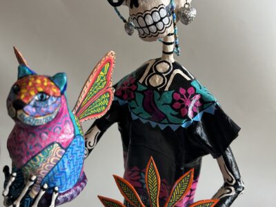 A papier-mache skeleton dressed as an elderly woman, holding a cat with wings