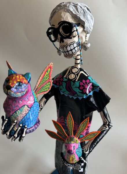 A papier-mache skeleton dressed as an elderly woman, holding a cat with wings