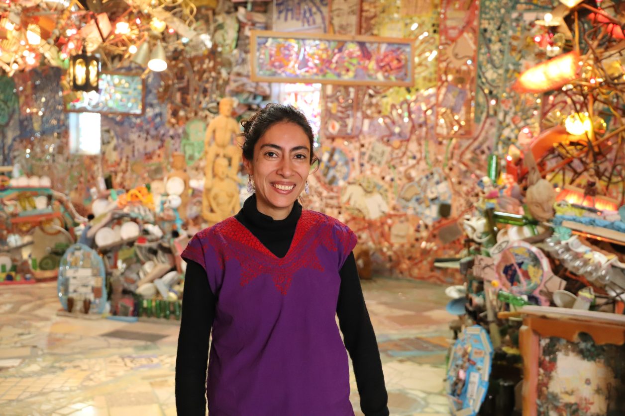 Artist Ivette Chaires smiles in a large mosaicked room at the Magic Gardens Studio