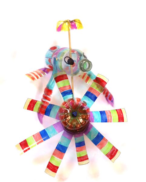 Two brightly colored garden ornaments made out of plastic bottles. One look like a flying fish with a propeller on its head. The other looks like a pinwheel.