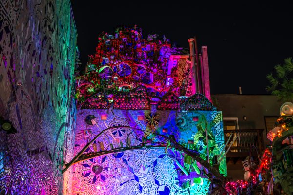 A nighttime view of a mosaicked outdoor wall lit up with colorful lights.